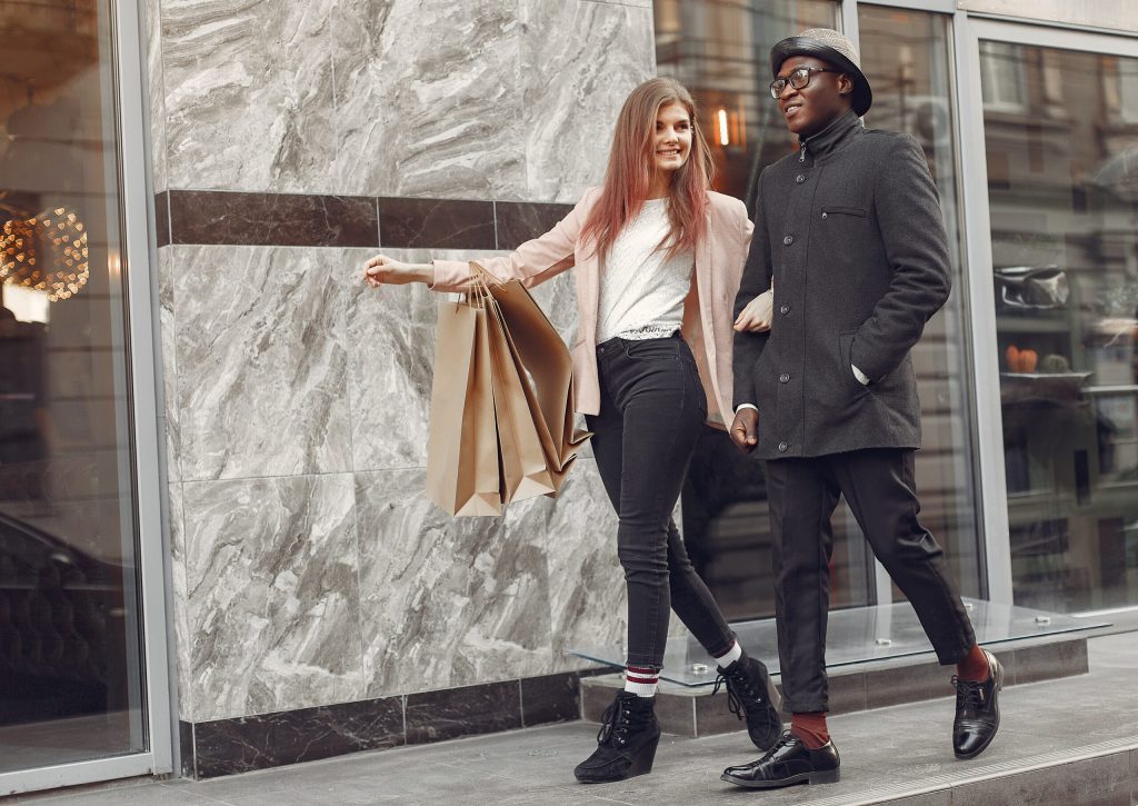 Stylish man and woman walking with shopping bags, showcasing confidence and inclusivity in modern promotional modeling.