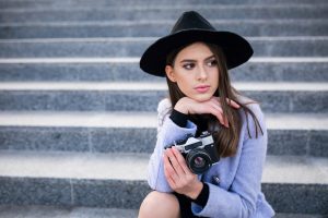 Young female model sitting on steps, holding a camera and looking thoughtful before her first modeling shoot with USA Models.